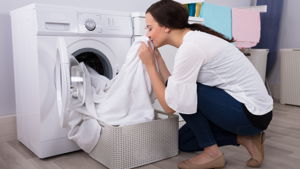 mulher em frente a maquina de lavar, cheirando toalhas