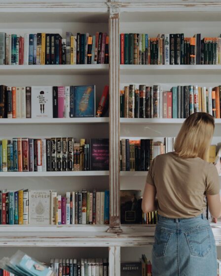 woman in beige shirt and blue denim jeans standing in front of books