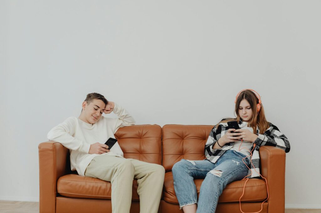 a boy and a girl sitting on sofa with smart phones in hands