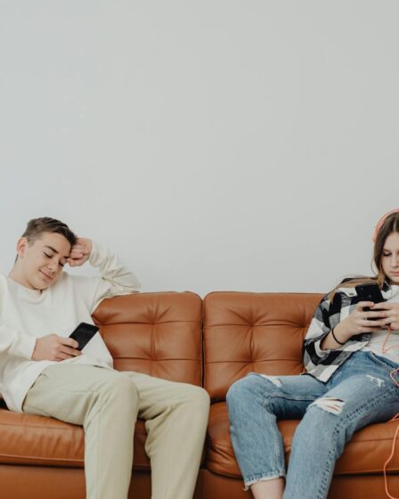 a boy and a girl sitting on sofa with smart phones in hands