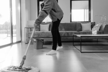 a grayscale photo of a person mopping the floor