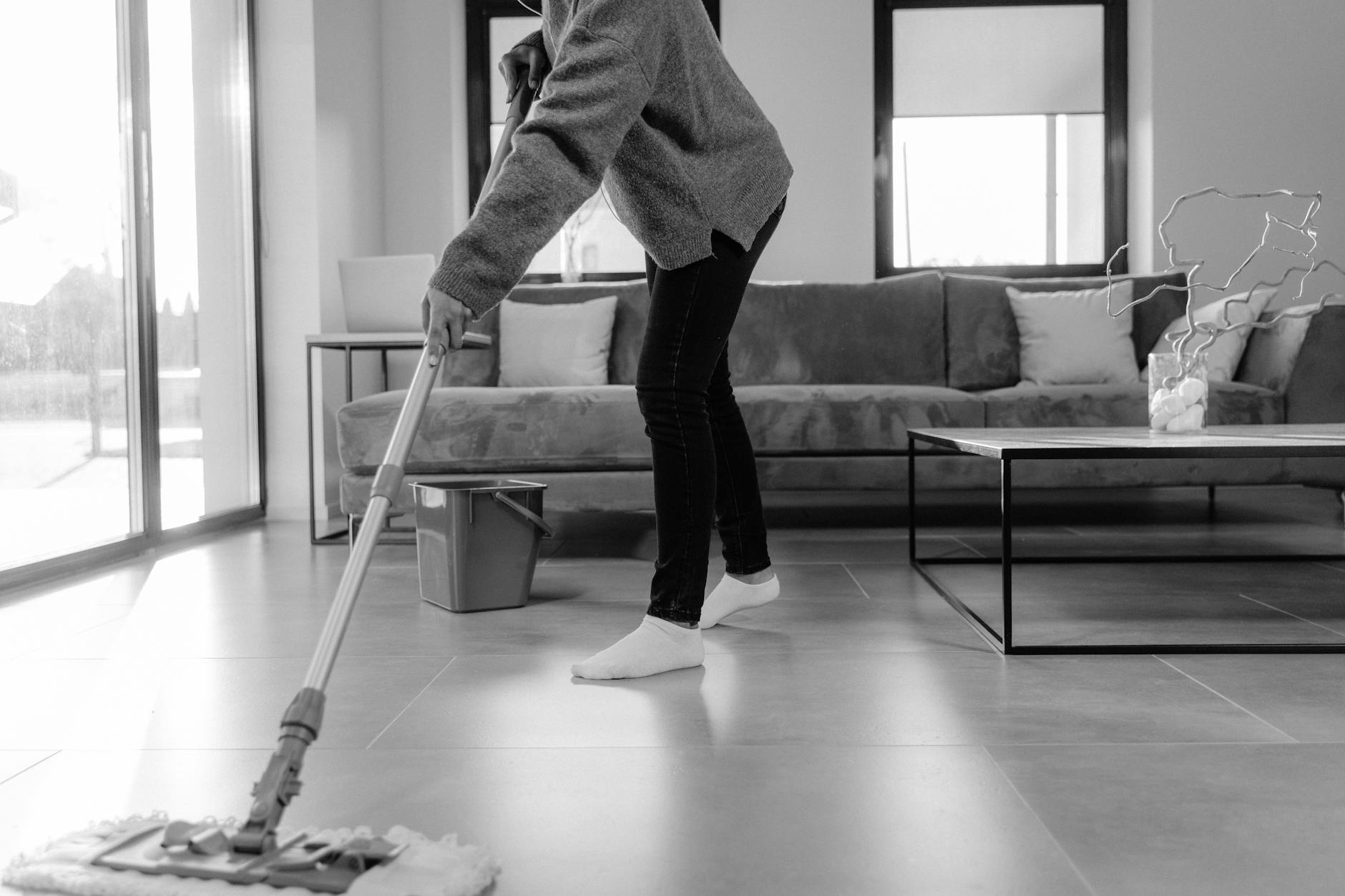 a grayscale photo of a person mopping the floor