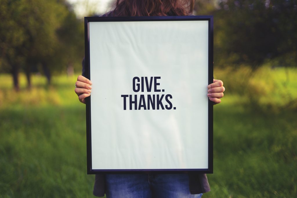 Mulher segurando um quadro com a frase em inglês "Give Thanks"