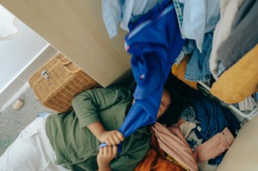 anonymous black girl lying on stack of clothes in bedroom