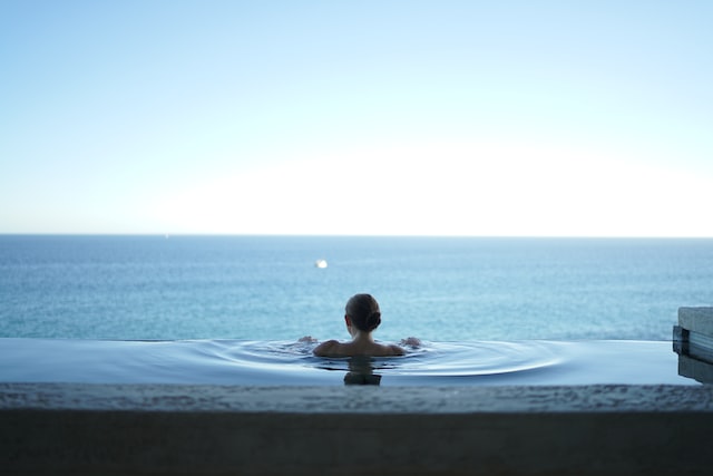 Mulher em piscina de fundo infinito contemplando o mar.