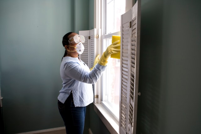 Senhora com máscara e óculos de proteção, fazendo limpeza doméstica para alérgicos