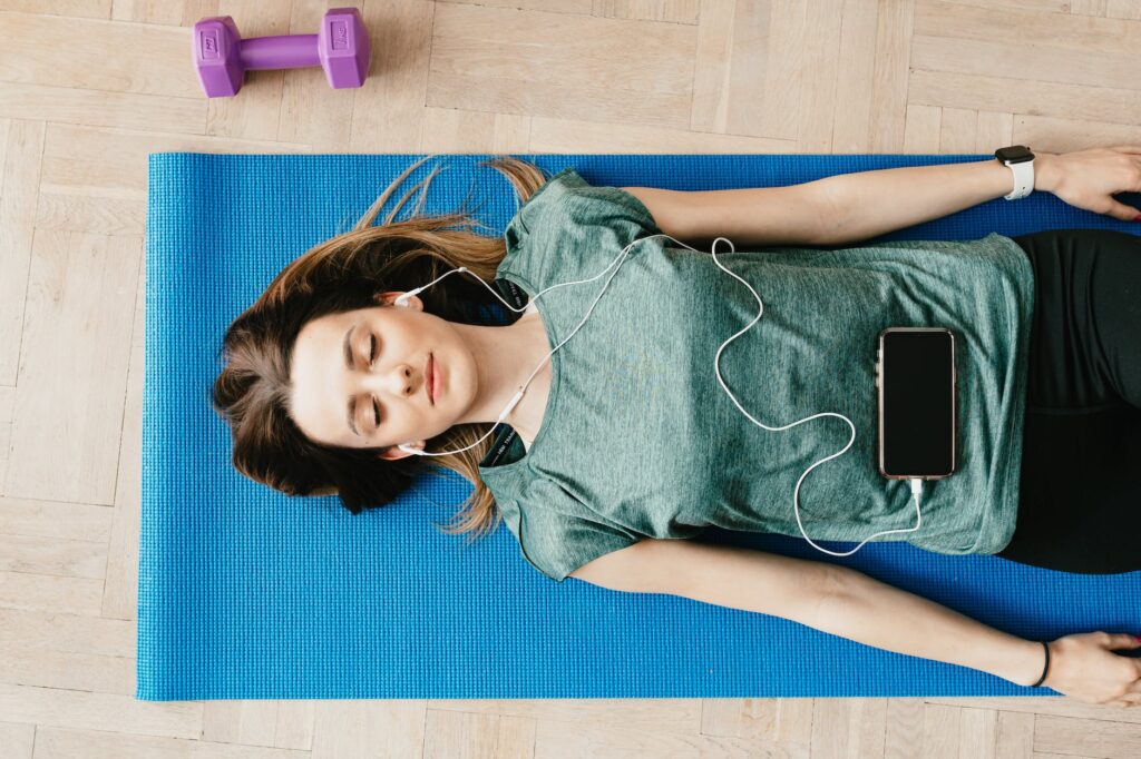 peaceful woman in earphones resting in shavasana pose at home
