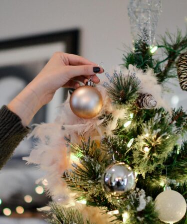 person holding beige bauble near christmas tree