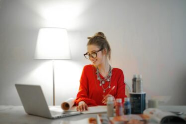 woman in red long sleeve shirt looking at her laptop