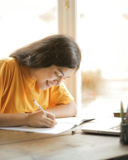 woman in yellow shirt writing on white paper