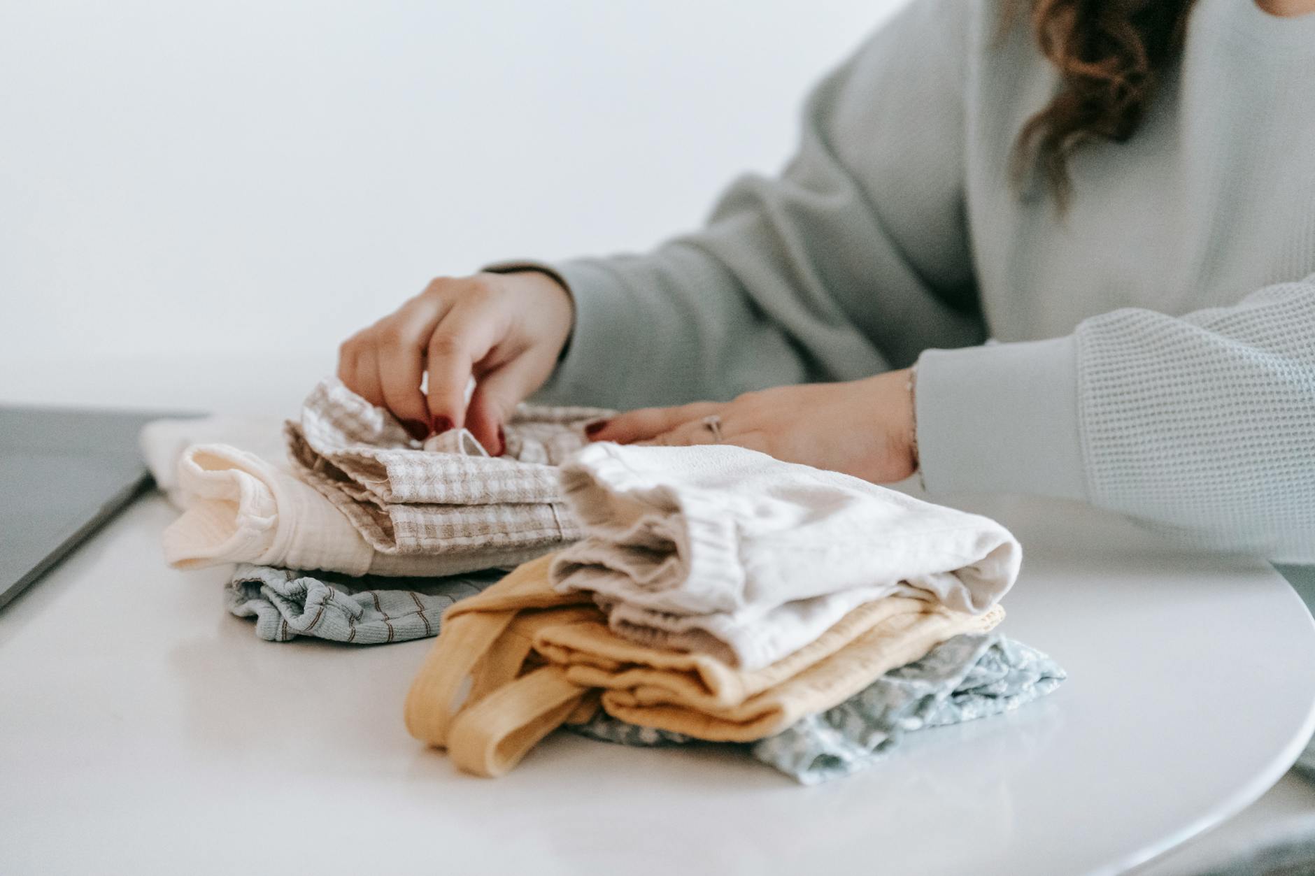 unrecognizable woman arranging baby clothes at table