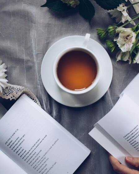 white ceramic teacup with saucer near two books above gray floral textile